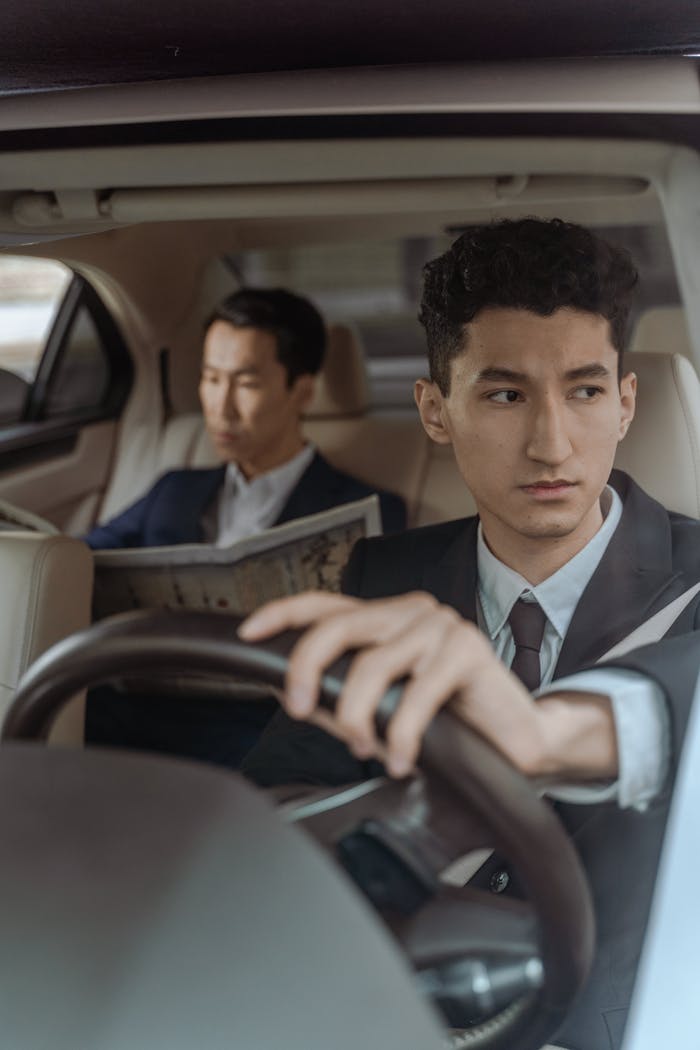 our-story Professional chauffeur driving with attentive passenger reading in a luxury car interior.