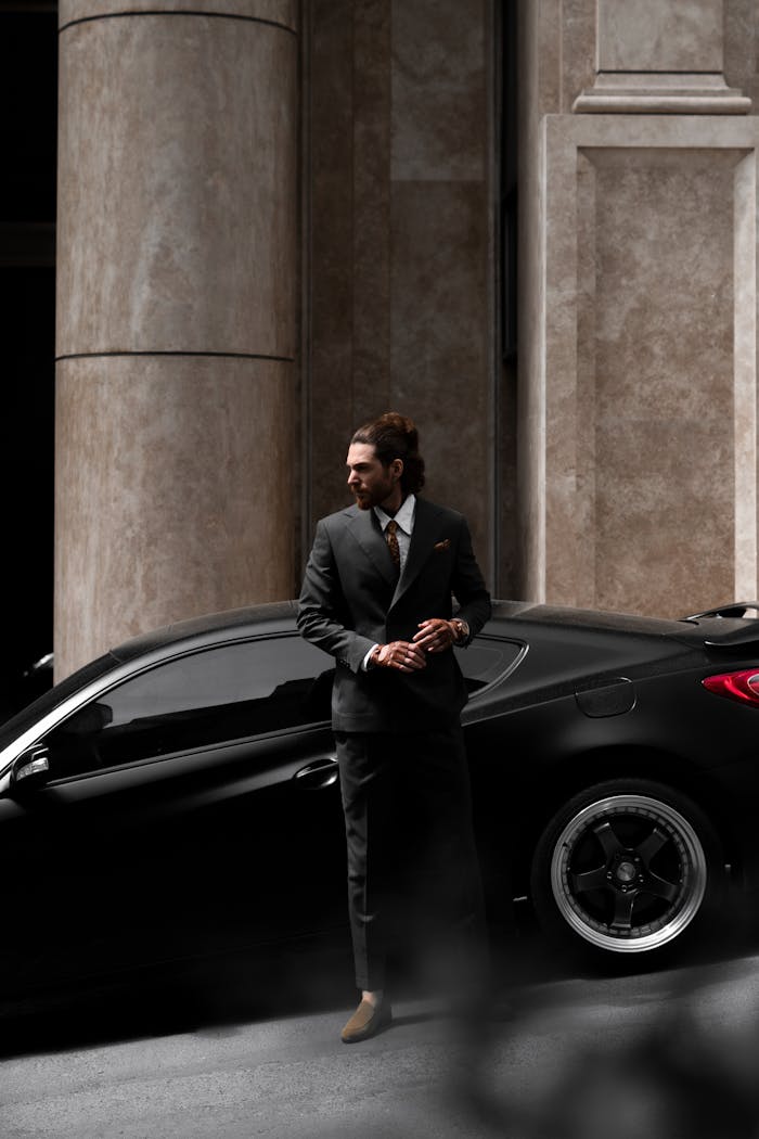 who-we-are Well-dressed man in formal suit stands by a luxury car on an urban city street.